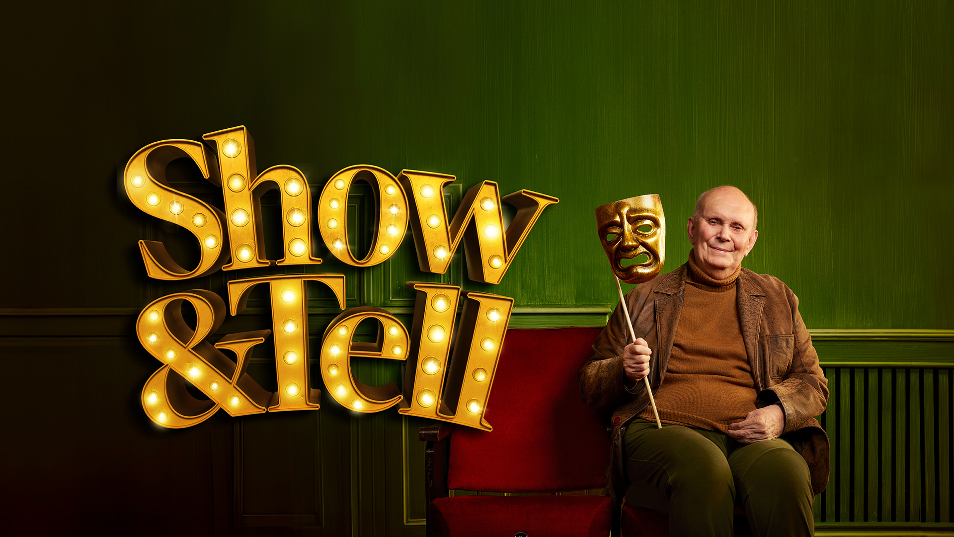 Production image for Show and Tell. Playwright and Director Alan Ayckbourn sits on red velvet theatre chairs holding a gold theatrical mask in front of a green background.