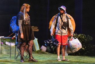 A young couple carrying lots of different camping equipment stare intensely at each other as if they are about to have a confrontation