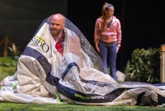 A man looks aggrieved as he struggles to put up a tent and appears to be stuck inside it