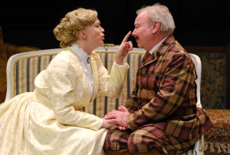 A woman in period dress flirts with a moustachioed man in a checkered suit